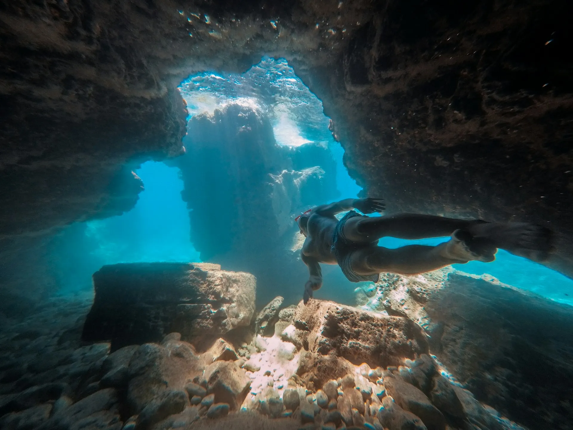 Snorkeler exploring an underwater cave with light streaming through
